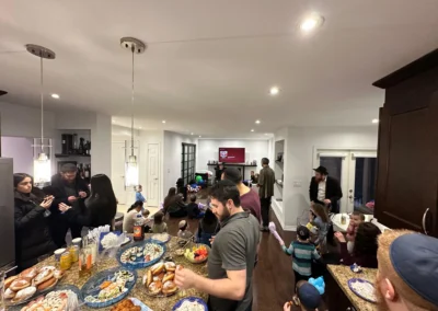 People gathered in an open kitchen and family room, with platters of sushi, doughnuts and fruit on the island and children playing
