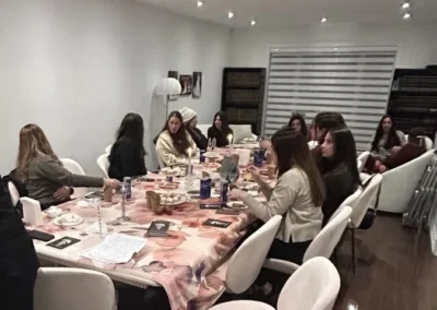 Women seated around a long dining table with a floral tablecloth and lit candles