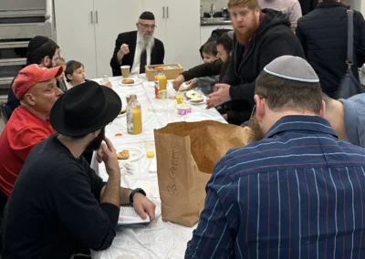 Men and children sharing bagels and orange juice around a long table