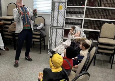 Children in costumes, one dressed as Batman, watching a performer balance a ball on his face