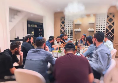 Men in kippot gathered around a dining table, with wine racks behind them