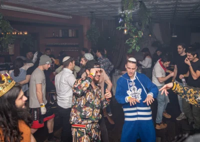 People in costumes dancing at a lively party, one in a Toronto Maple Leafs onesie and another in a toy crown