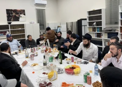 Men seated around a long table with fruit, snacks and drinks, in a room lined with bookshelves